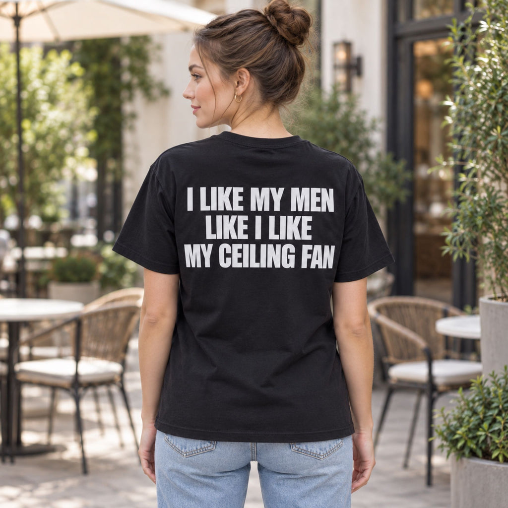 I Like My Men Like I Like My Ceiling Fan black graphic tee back print on female model at a cafe terrace
