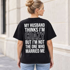 Black My Husband Thinks I'm Crazy graphic T-shirt worn by a female model, rear view with white lettering and outlined CRAZY