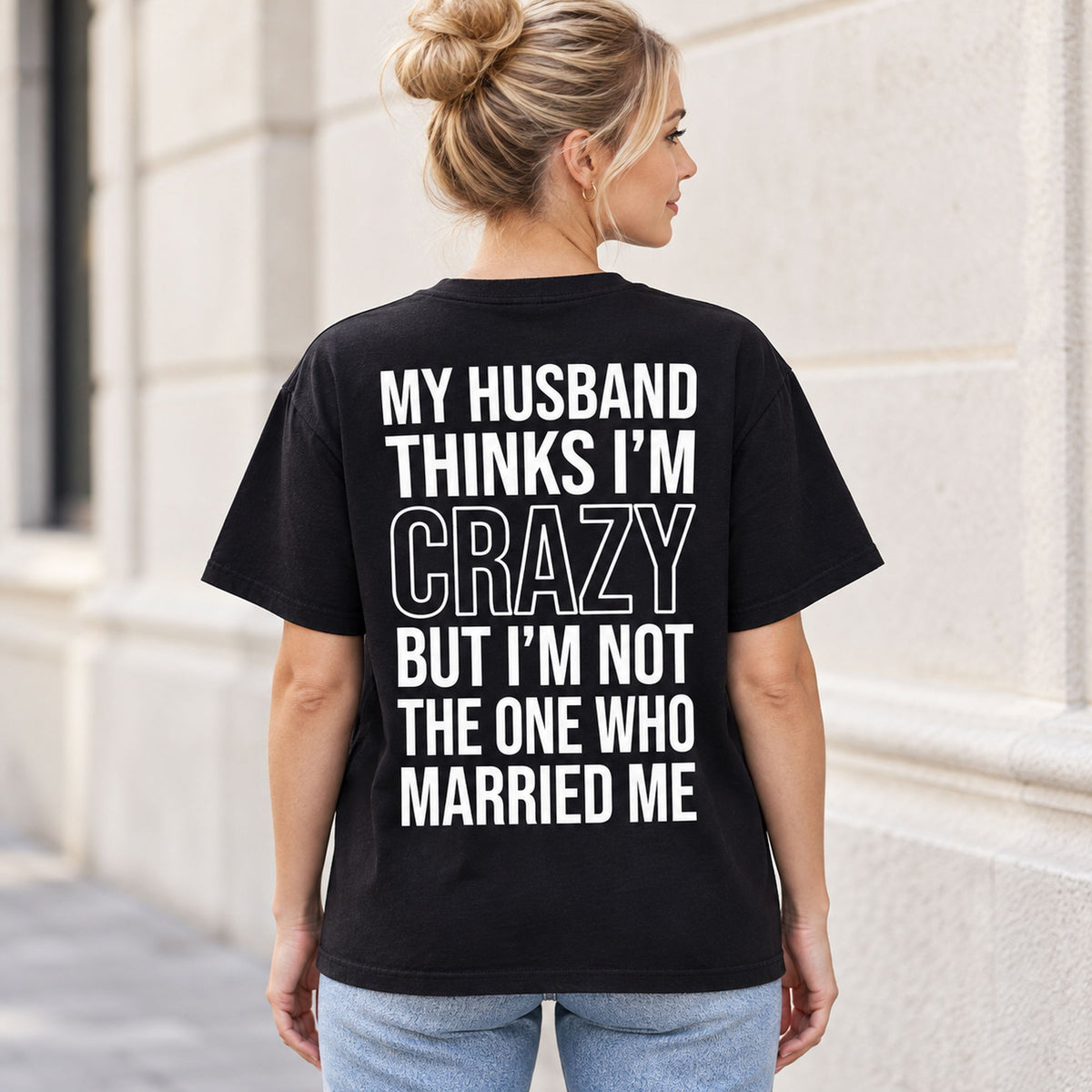 Black My Husband Thinks I'm Crazy graphic T-shirt worn by a female model, rear view with white lettering and outlined CRAZY