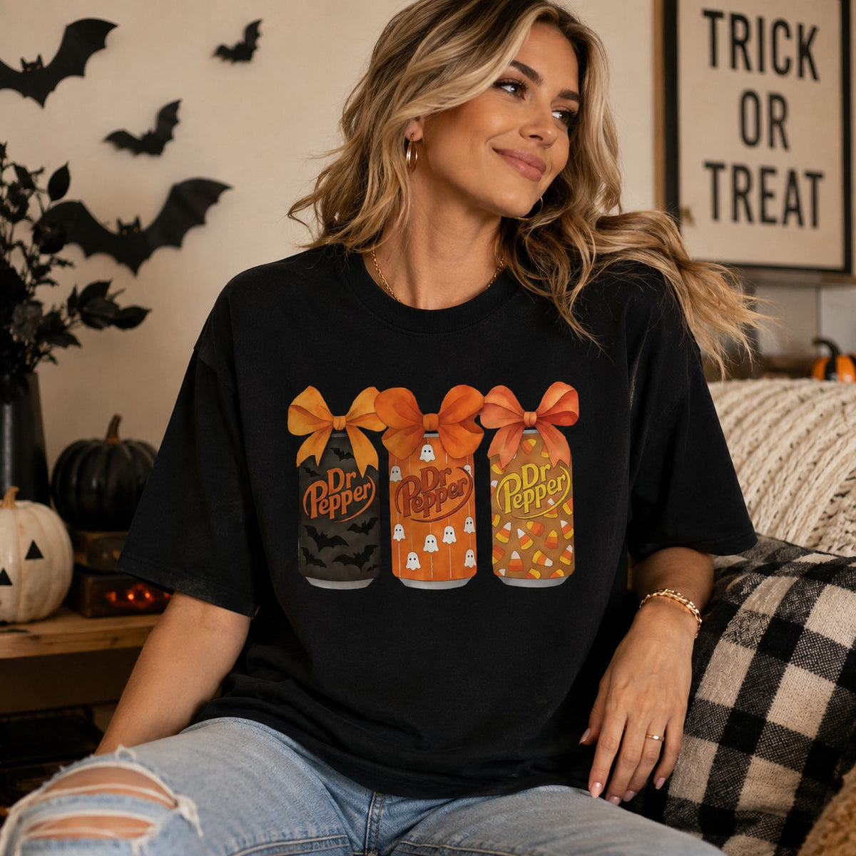 Female model wearing black Dr Pepper Halloween bow cans front-print graphic tee in a decorated fall living room