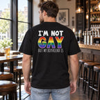 I'm Not Gay But My Boyfriend Is black graphic tee, back-facing model with rainbow lettering in a casual bar setting