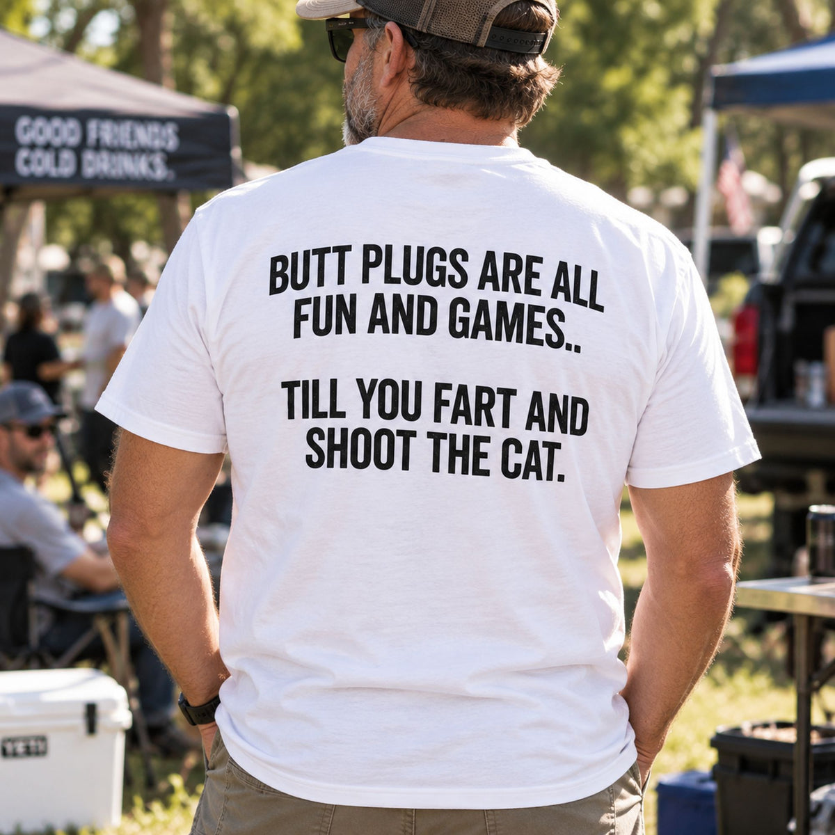 Butt Plugs Are All Fun And Games white back-print graphic tee on a standing male model at an outdoor gathering