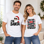 White I'm Santa and I'm So Good Santa Came Twice graphic tees shown on a couple in a Christmas setting