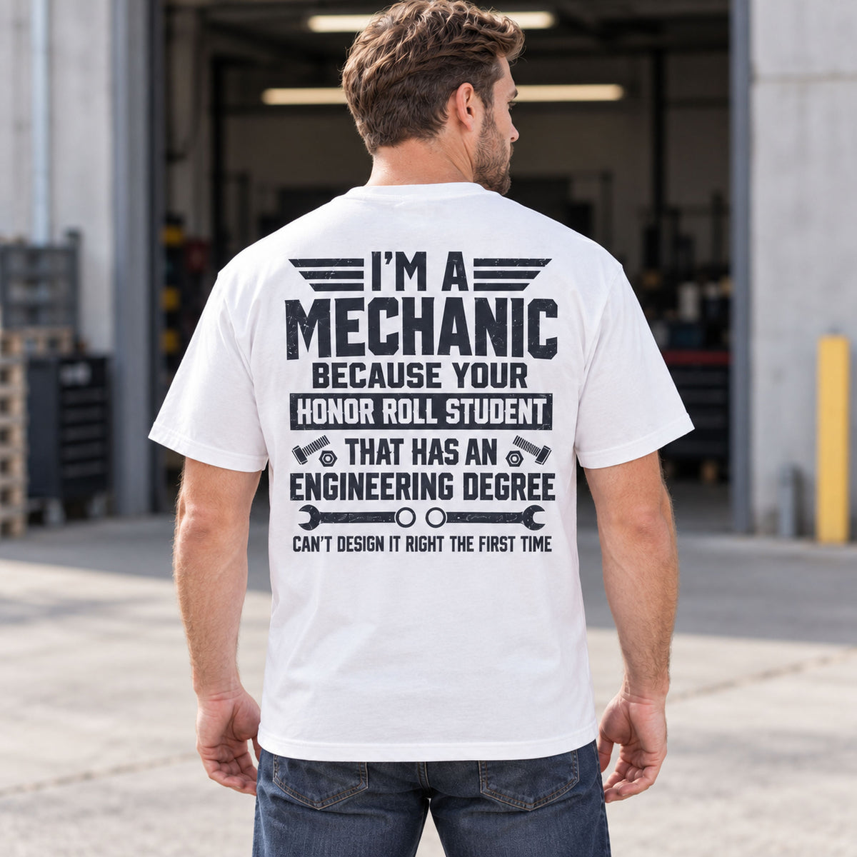 I'm A Mechanic humorous back-print T-shirt in white, rear-view male lifestyle model at a workshop