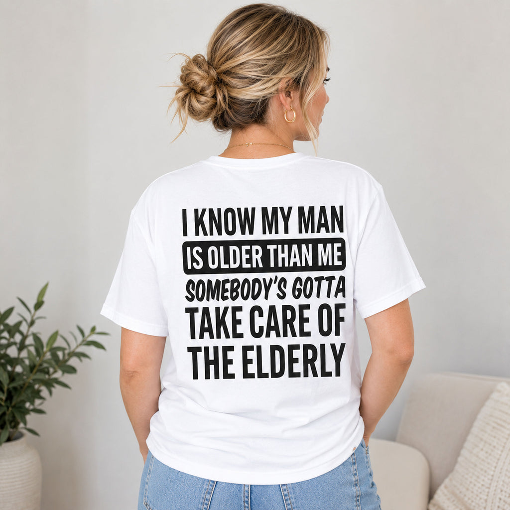 I Know My Man Is Older Than Me relationship humor graphic tee on a woman in white, indoor rear view