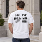 Say Eye Spell Map Say Ness funny wordplay back print white T-shirt male model beside a stone building