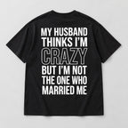Black My Husband Thinks I'm Crazy T-shirt back flat lay with six lines of white text and large outlined CRAZY