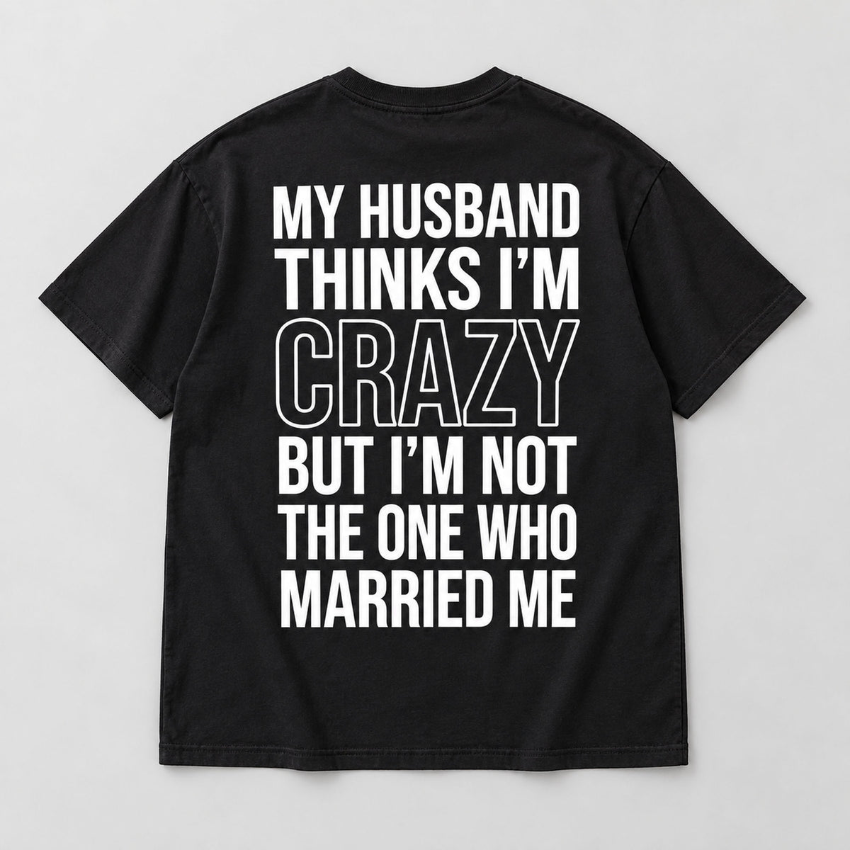 Black My Husband Thinks I'm Crazy T-shirt back flat lay with six lines of white text and large outlined CRAZY