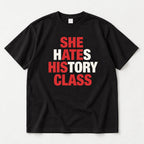 She Hates History Class black graphic T-shirt flat lay with red letter accents across four lines