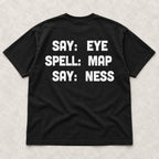 Say Eye Spell Map Say Ness white lettering on a black T-shirt back flat lay on a textured surface