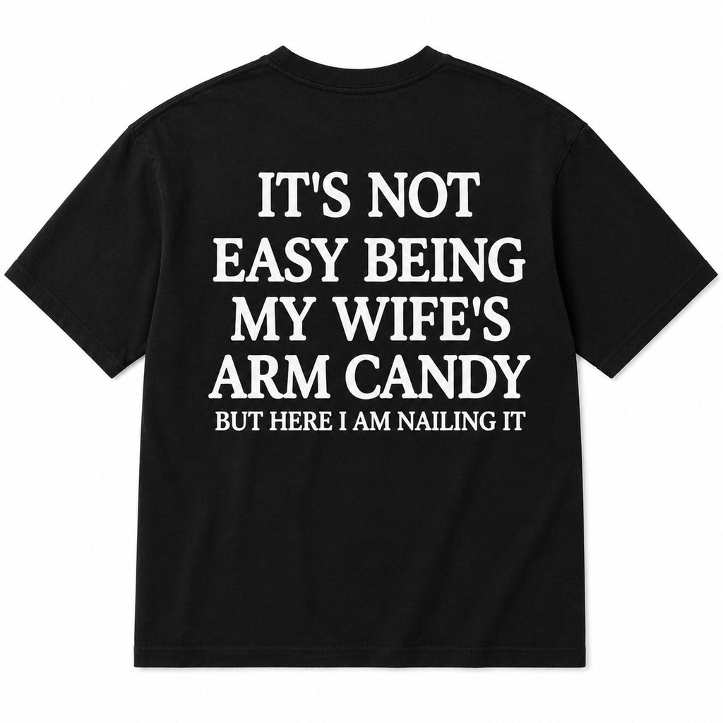 It's Not Easy Being My Wife's Arm Candy black graphic tee back-print flat lay
