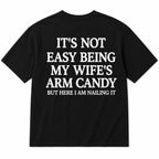 It's Not Easy Being My Wife's Arm Candy black graphic tee back-print flat lay