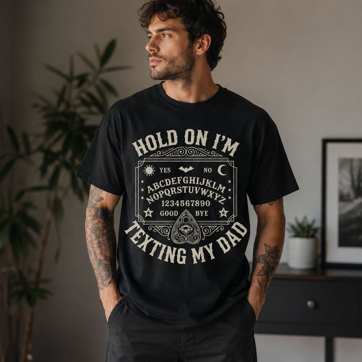 Male model wearing black Hold On I'm Texting My Dad Ouija board graphic tee, front view