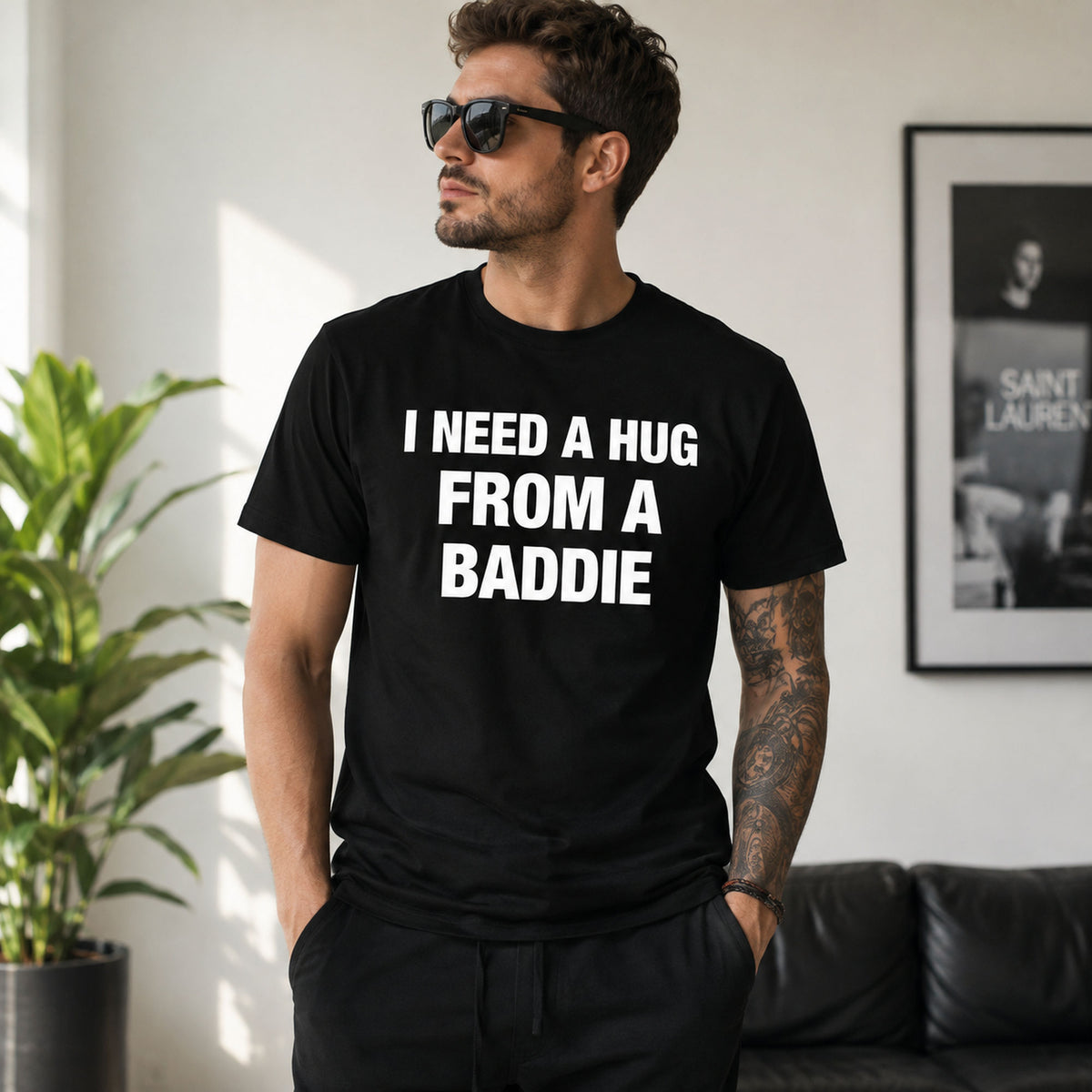 Male model wearing black I Need a Hug From a Baddie funny front-print graphic tee in a bright living room