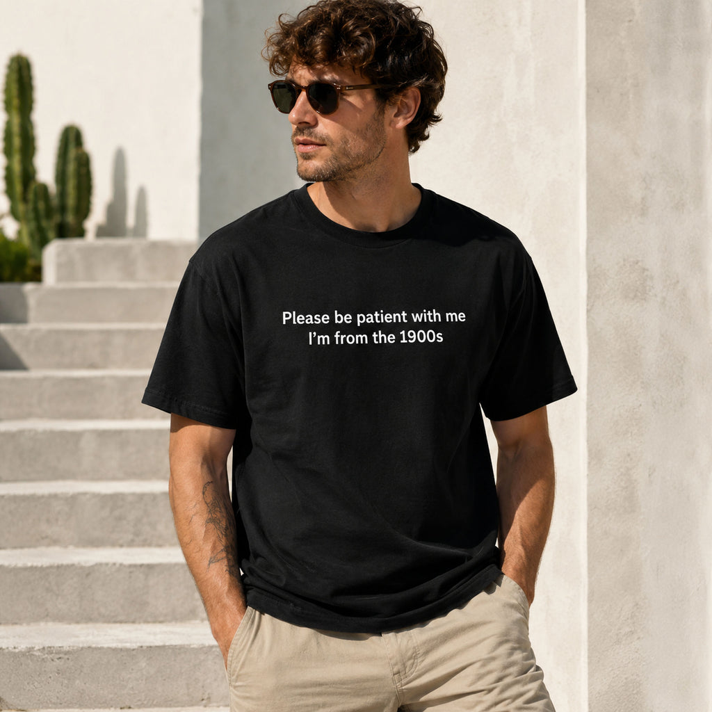 Male model wearing black Please Be Patient I'm From the 1900s funny front-print graphic tee by sunlit white resort stairs
