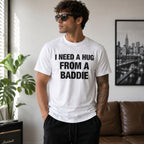 Male model wearing white I Need a Hug From a Baddie funny front-print graphic tee in a bright living room